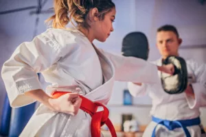 young female karate player with trainer using focus mitts during training